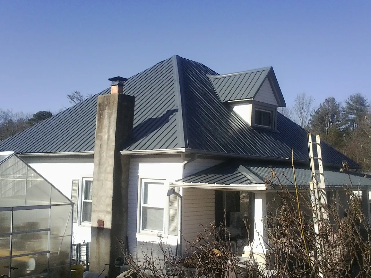 Dark blue standing seam metal roof on a white farmhouse with dormer — Slate & Tile Roof Repair by Roofing Brothers in Massapequa