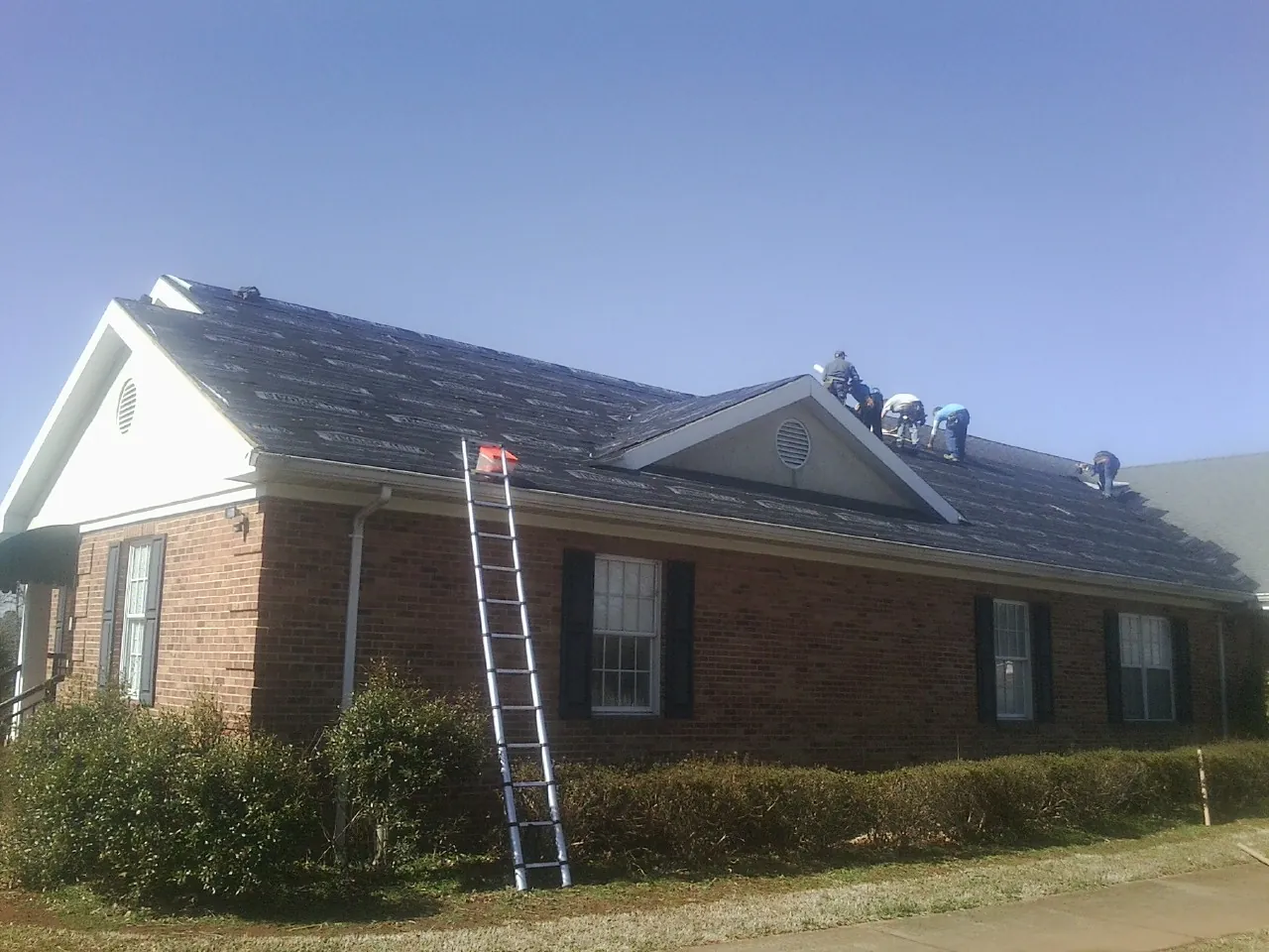 Crew tearing shingles off a brick ranch roof with a ladder set — Emergency Roof Repair work by our crew in Massapequa