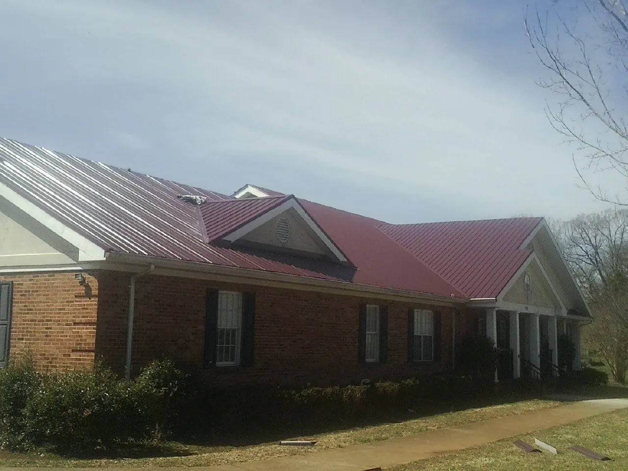 Red metal roof with gabled entries on a long brick building, from a Hail Damage Roof Repair job in Massapequa