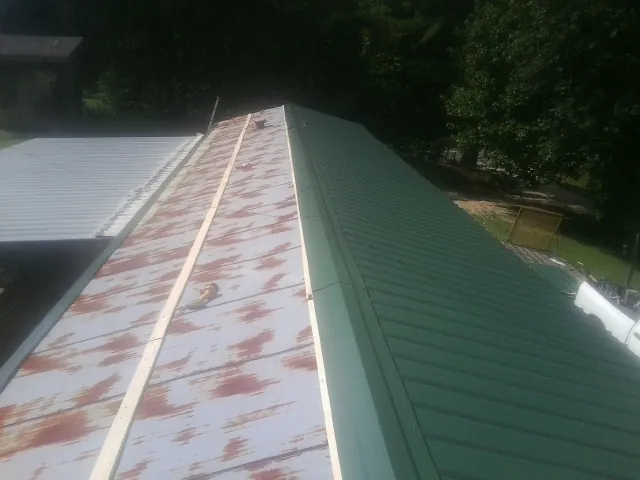Old rusted panels beside newly installed green metal roofing — Wind Damage Roof Repair by Roofing Brothers in Massapequa