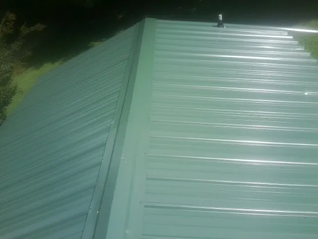 New green metal panels meeting at the ridge of a roof — Flat Roof Repair work by our crew in Massapequa