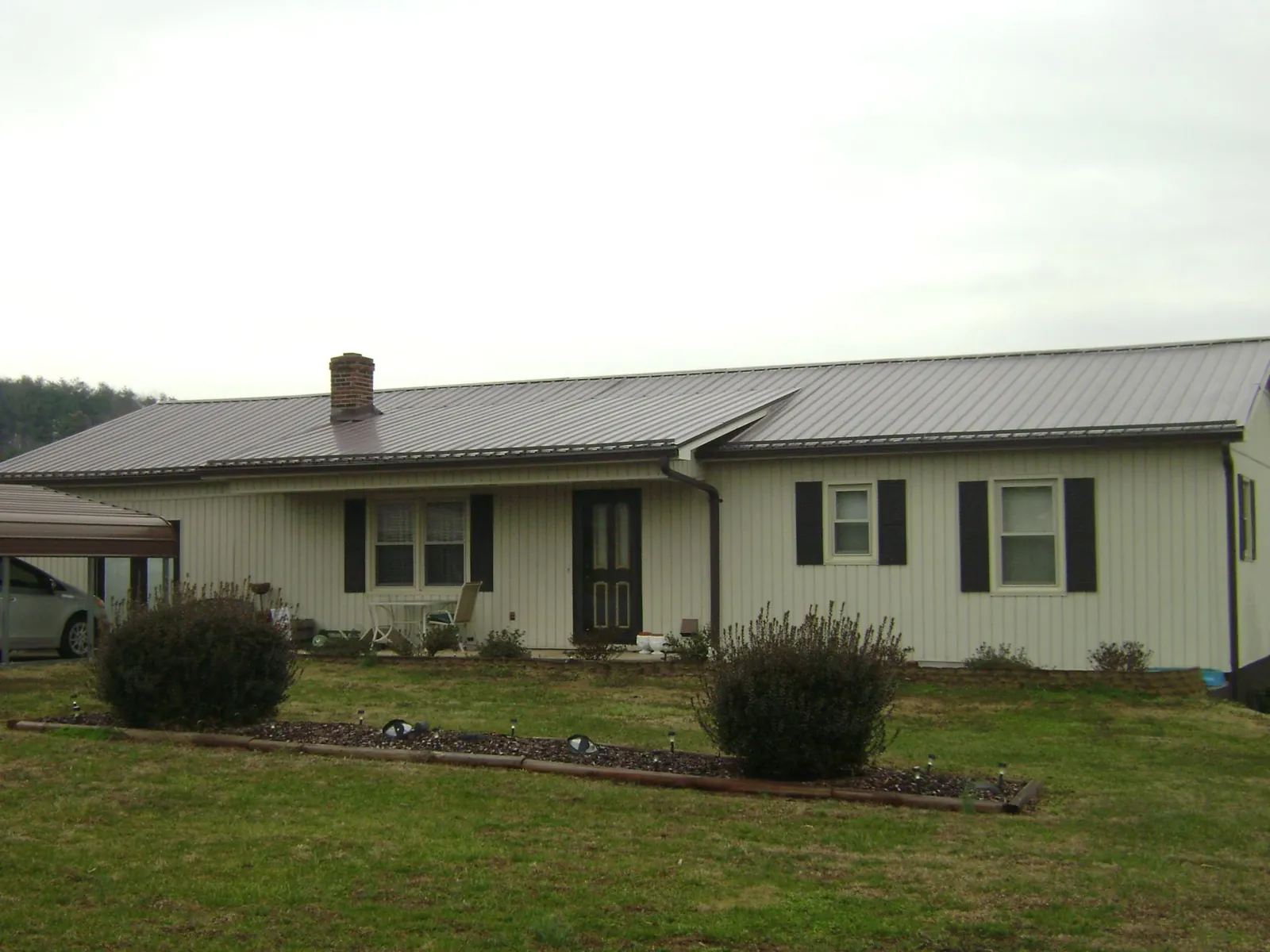 Brown metal roof on a cream sided ranch home with a brick chimney in Massapequa