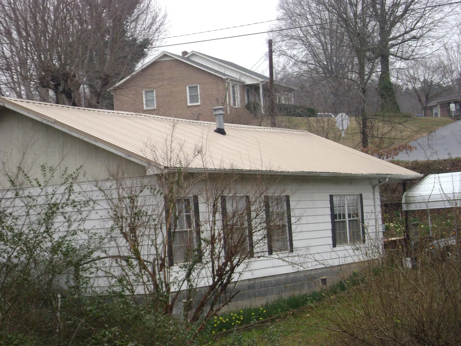 Tan metal roof on a white sided house set into a hillside — Commercial Roofing by Roofing Brothers in Massapequa